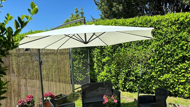 Une terrasse avec des meubles d’extérieur, un grand parasol et des plantes en pot.