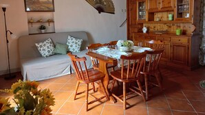 Un coin repas chaleureux avec une table en bois dressée pour quatre personnes, entourée de chaises en bois. On aperçoit, au fond, un buffet en bois doté de portes en verre.