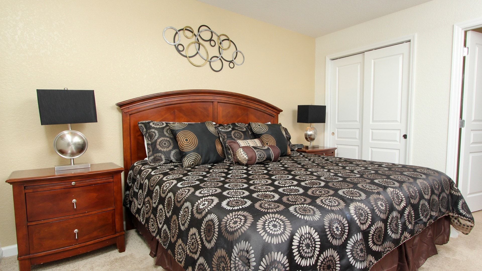 A bedroom with a large bed, two nightstands, a wooden dresser, a wall art piece, and a door.