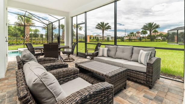Un patio iluminado por el sol con mobiliario de mimbre, una piscina y vistas a un paisaje verde y exuberante.
