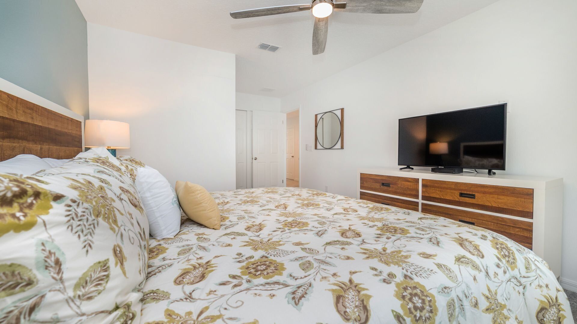 Une chambre à coucher comprenant un lit, un téléviseur, un ventilateur de plafond et une commode.