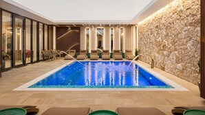 A modern indoor pool area with lounge chairs and a stone wall. - Ramada by Wyndham Zalau (Zalau)