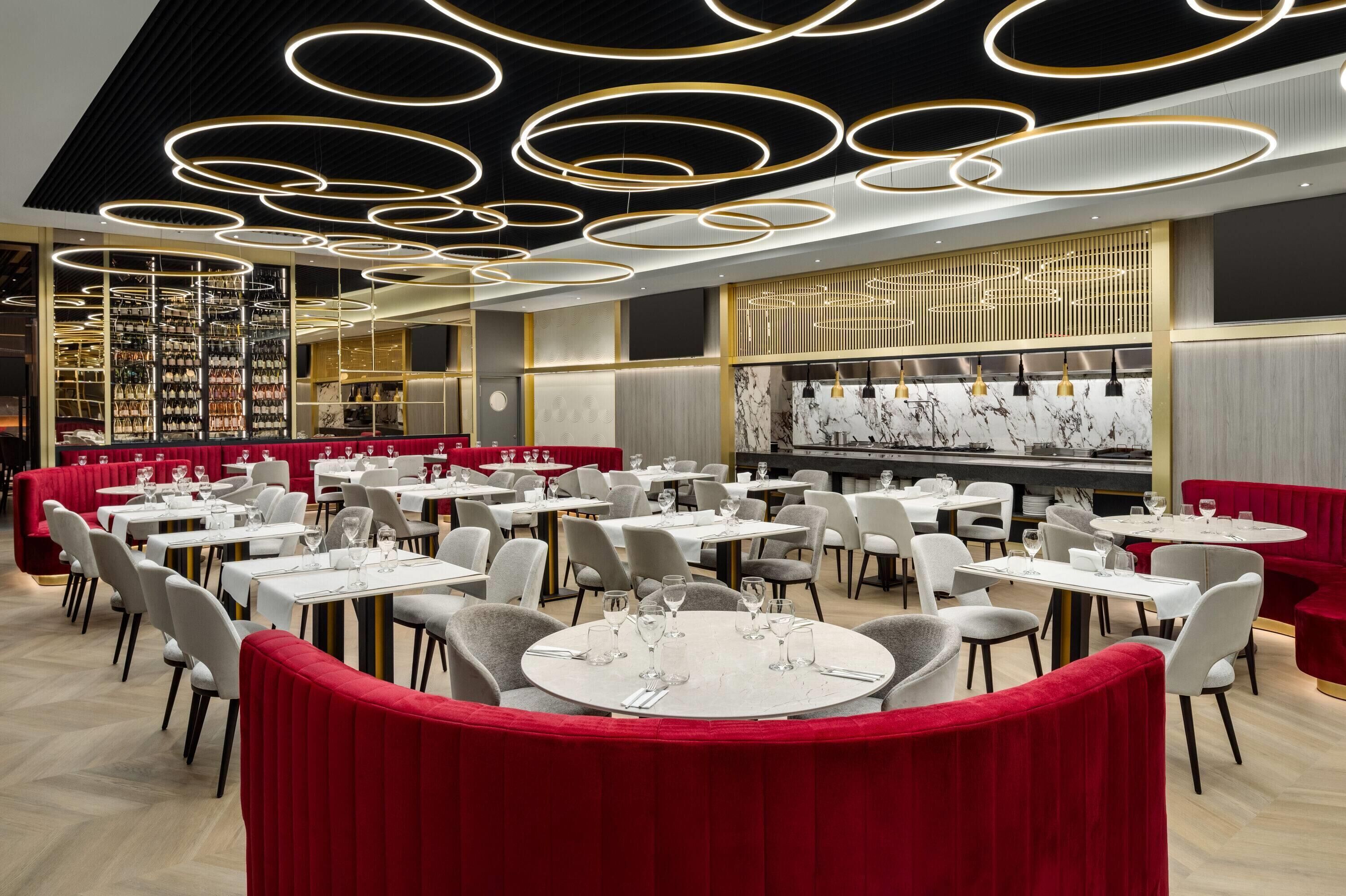 Un restaurante moderno con mesas redondas, cabinas tapizadas en rojo y un techo con lámparas circulares.