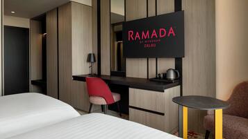 Una habitación de hotel moderna con una cama, un escritorio, una silla, una mesita y un televisor que muestra 'RAMADA BY WYNDHAM ZALAU'.