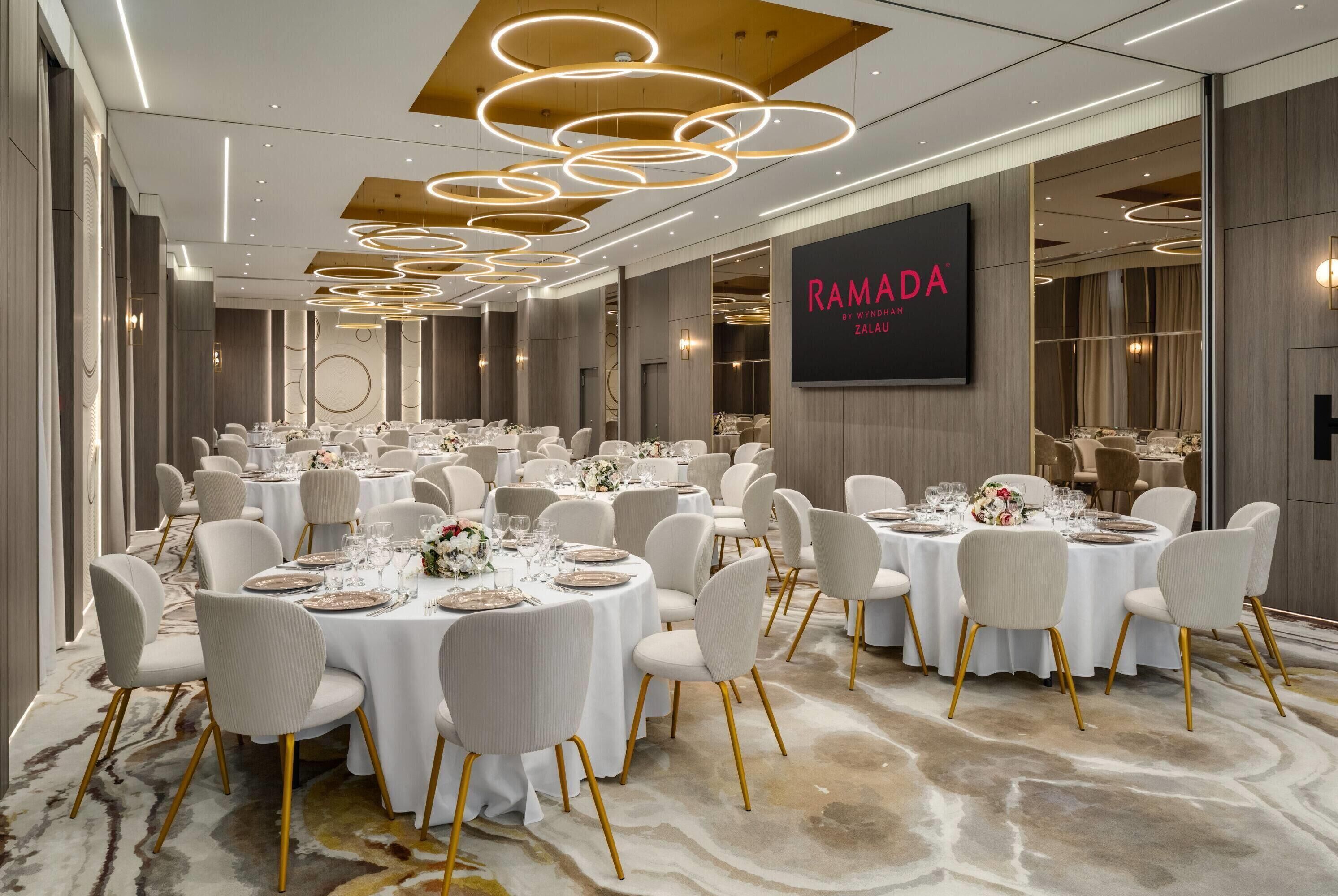 A banquet hall with round tables set for dining, featuring gold chairs and white tablecloths.