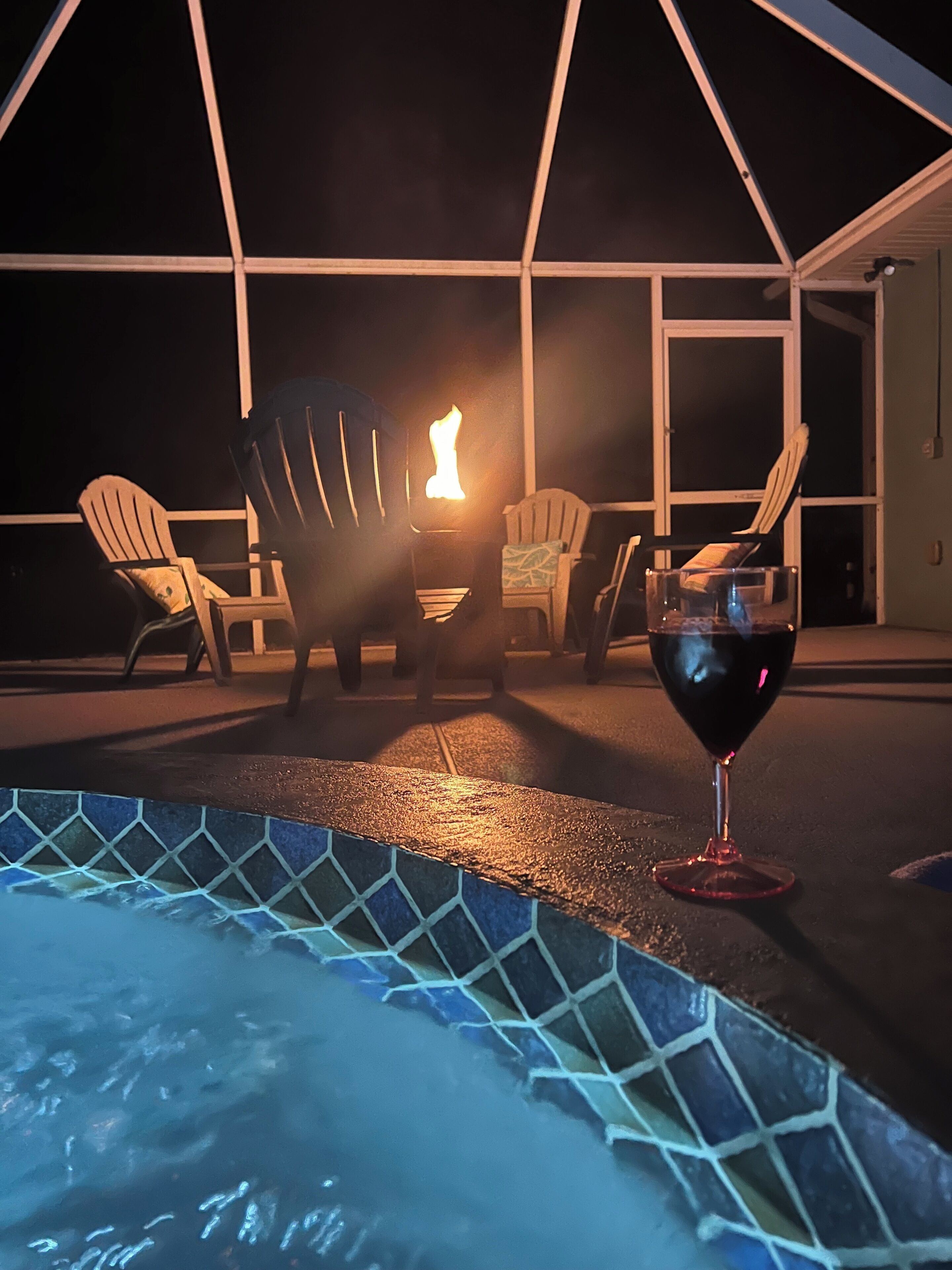 Ein Whirlpool mit gefliestem Rand, zwei Adirondack-Stühle und ein Glas Rotwein unter einer Zeltdachkonstruktion.