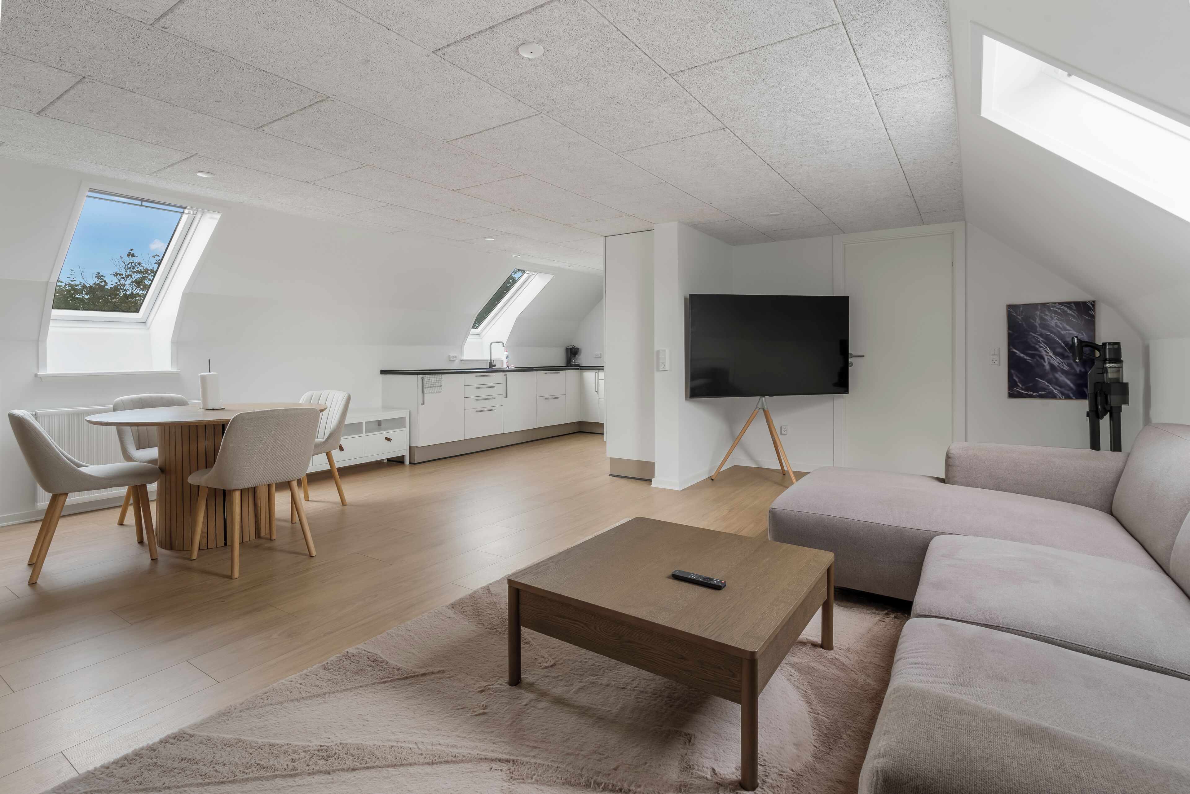 Una sala moderna con televisor de pantalla plana, un sofá, una mesa de centro y un comedor con sillas y una mesa.