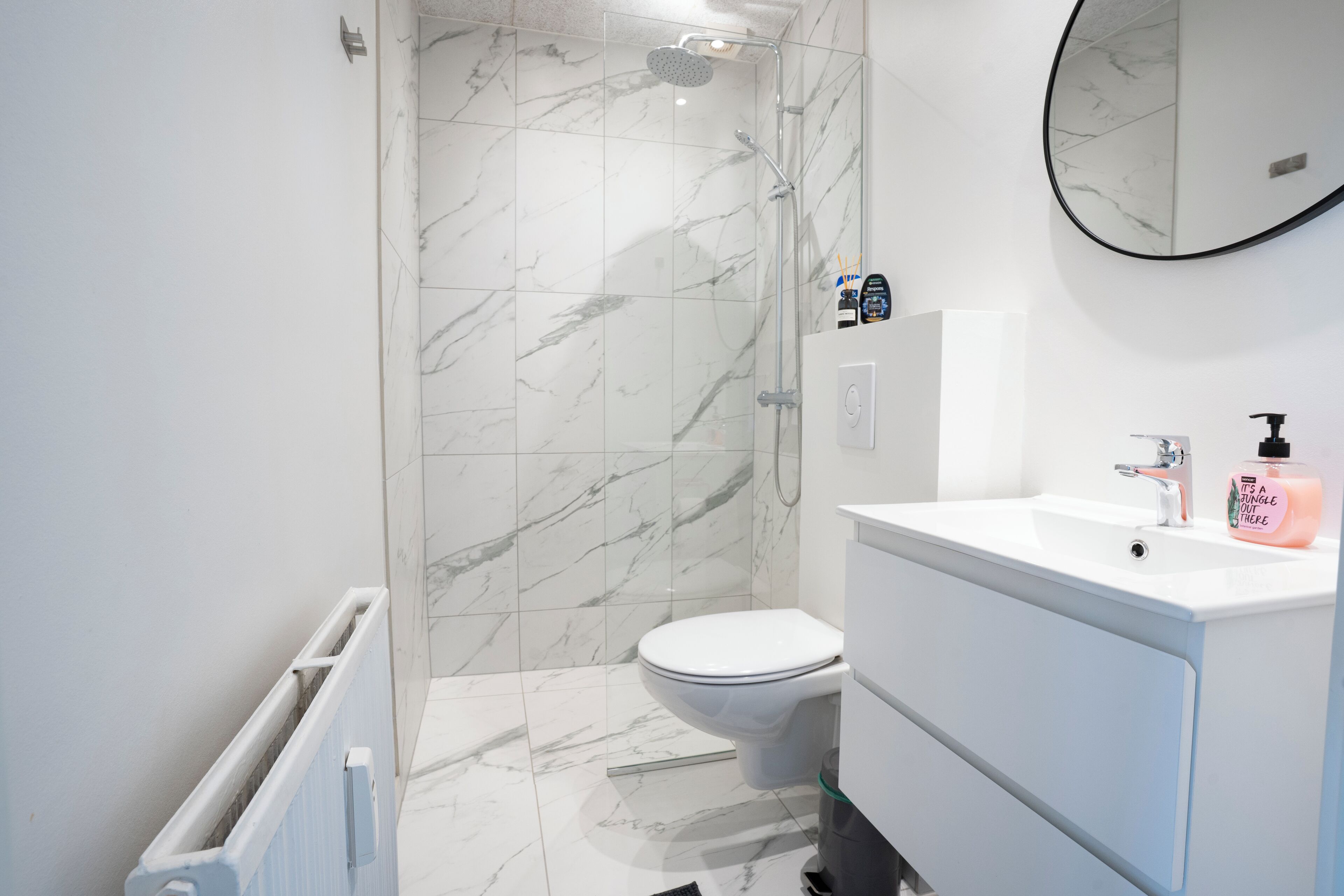A modern bathroom with a white marble shower, a toilet, and a sink with a mirror above it.