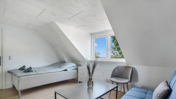 Un dormitorio tipo loft moderno con techo inclinado, cama, sofá, mesa y ventana con vistas.