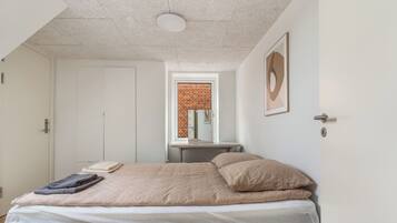 A bedroom with a bed, a window with a view of a brick wall, a door, and a framed picture on the wall.