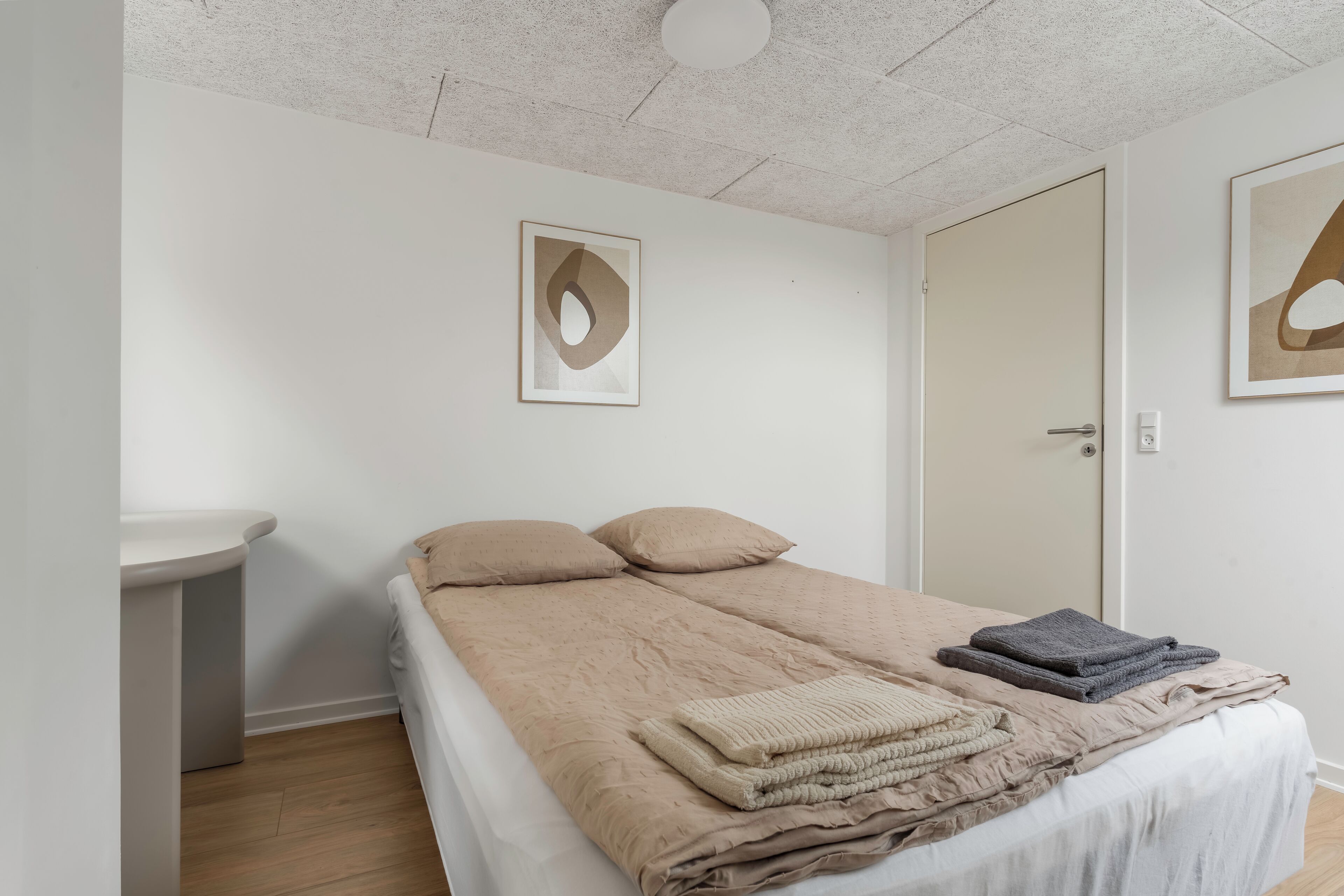 A bedroom with a bed, a bedside table, a wall-mounted artwork, and a door.