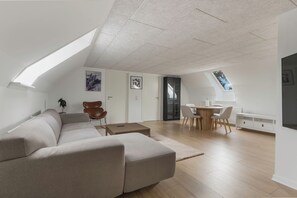 Un espace de vie moderne doté d’un haut plafond, d’un canapé d’angle, d’un coin repas avec une table ronde et d’une bibliothèque intégrée.