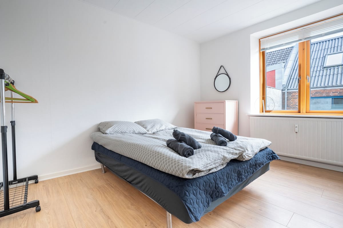 A bedroom with a bed, a dresser, a radiator, and a window with a view of a building.