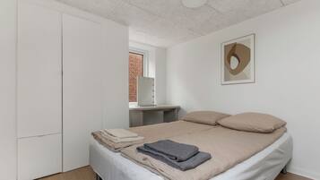 A bedroom with a bed, a wardrobe, a vanity with a mirror, and a framed abstract artwork on the wall.