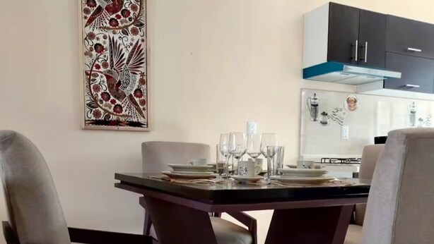 A dining area with a table set for four, surrounded by chairs. A kitchen with modern appliances is visible in the background. - Spacious and private apartment (Oaxaca de Juárez)