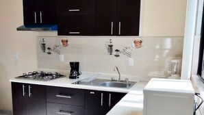 A compact kitchen with dark cabinets, a white countertop, a built-in stove, a sink, and a white refrigerator. - Spacious and private apartment (Oaxaca de Juárez)