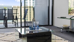 A modern living room with a glass coffee table, a decorative vase, and a television on a stand. - Cozy 1 Bedroom + Study Ocean View Unit - Q Stay (Surfers Paradise)