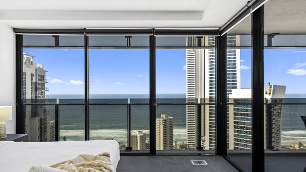 A hotel room with a large balcony, a bed, and a view of the ocean and city skyline. - Cozy 1 Bedroom + Study Ocean View Unit - Q Stay (Surfers Paradise)