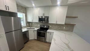 A modern kitchen with white cabinets, stainless steel appliances, a marble countertop, and a wooden floor. - Stunning Waterfront Condo, Fully Remodeled – Bring Your Boat, No Fixed Bridges! (Boca Raton)