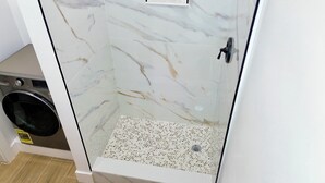 A bathroom with a glass-enclosed shower, a built-in washing machine, and a tiled floor. - Stunning Waterfront Condo, Fully Remodeled – Bring Your Boat, No Fixed Bridges! (Boca Raton)