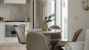 Una cocina moderna con refrigerador empotrado, una zona de comedor con sillas de mimbre y un amplio ventanal que proporciona luz natural.