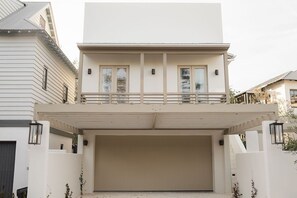 Une maison moderne à deux étages, dotée d’un garage fermé, de grandes fenêtres et d’un balcon.