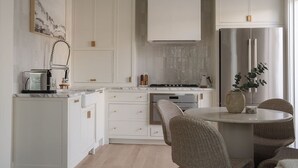 Una cocina moderna con armarios blancos, un refrigerador de acero inoxidable y una mesa de comedor redonda con sillas de mimbre.