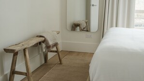 Un dormitorio con un banco de madera, un espejo grande y una cama con ropa de cama blanca.