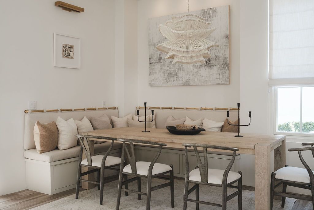 A dining area with a long table, cushioned seating, and a large abstract painting on the wall.