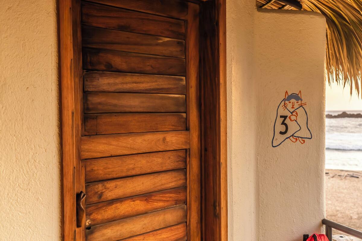 Una puerta de madera con listones horizontales, un letrero con el número 3 y vistas a la playa.
