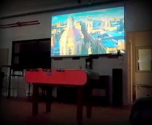 Ett rum med en stor skärm som visar en stadsbild, en röd bänk och en dörr.