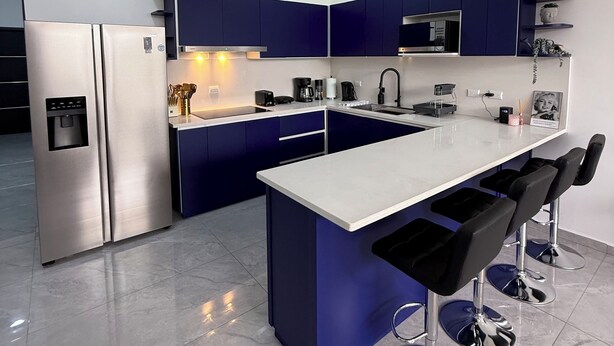 A modern kitchen with a central island, bar stools, and built-in appliances. - Casa Azul Jaco (Jaco)
