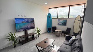 A modern living room with a large flat-screen TV, a sofa, a coffee table, and two surfboards. - Casa Azul Jaco (Jaco)