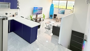 A modern kitchen with a central island, a dining area with a view, and a living space with a surfboard. - Casa Azul Jaco (Jaco)