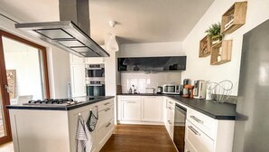 Een moderne keuken met witte kasten, een centraal eiland, roestvrijstalen apparatuur en een houten vloer.