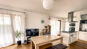 Een moderne keuken met een eethoek, houten vloeren en een groot raam met lichte gordijnen.