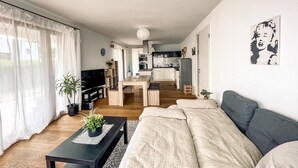 Een moderne woonkamer met een bank, een salontafel met planten, een televisie en een eethoek, met een keuken op de achtergrond.