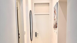Een gang met een houten vloer, een witte deur en een foto in een lijst aan de muur.