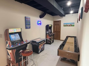 Une pièce avec une borne d’arcade, une table de billard et une porte.