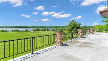 Un balcon doté d’une balustrade en métal, d’un pilier en briques et offrant une vue sur un lac et un paysage verdoyant.