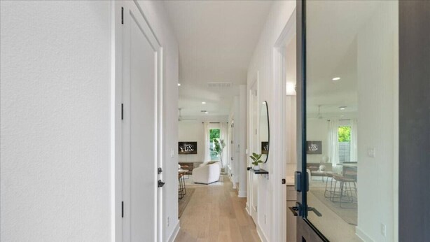 Un pasillo moderno con paredes blancas y suelo de madera, que conduce a un comedor con un separador de vidrio.