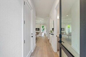 Een moderne hal met witte wanden en houten vloeren, die uitkomt op een eetgedeelte met een glazen scheiding.