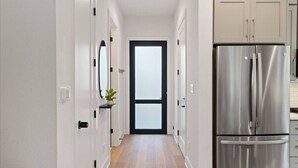 Una cocina moderna con electrodomésticos de acero inoxidable, piso de madera y vista al área de estar a través de una puerta de vidrio.