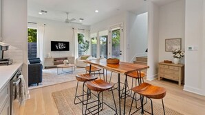 Un salón amplio con una mesa de comedor de madera y taburetes de bar, un sofá y un televisor montado en la pared.