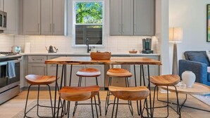 Una cocina moderna con armarios grises, una isla central con taburetes, una ventana con vistas a zonas verdes y una cafetera.