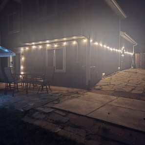 Un espace extérieur aménagé avec des tables et des chaises, une clôture en bois et un bâtiment décoré de guirlandes lumineuses.