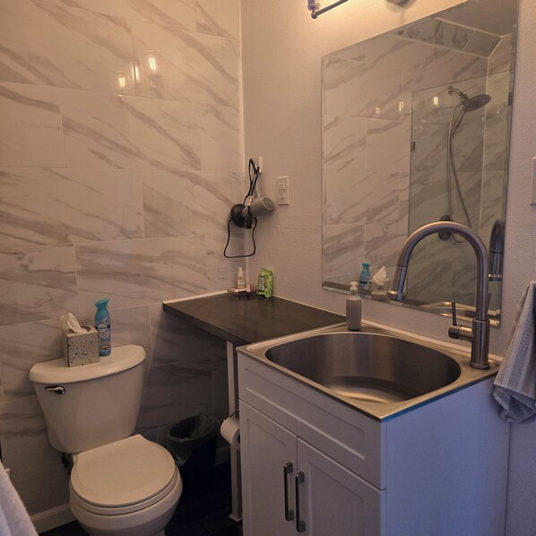 Un baño con inodoro, lavamanos, espejo y zona de ducha.
