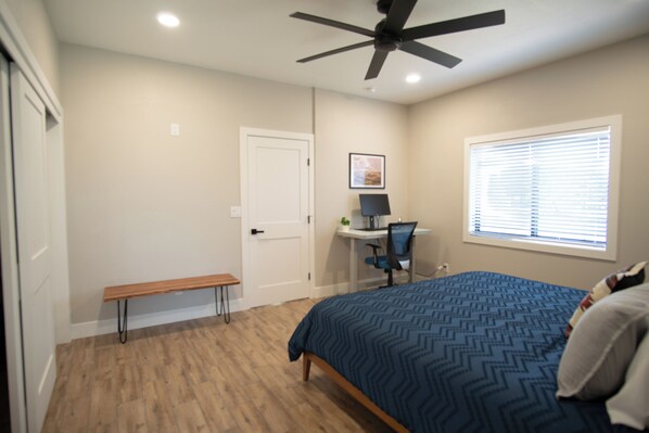 A bedroom with a bed, a desk, a chair, a bench, and a ceiling fan.