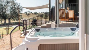 A hot tub on a balcony with a view of olive trees and a patio area with outdoor furniture.