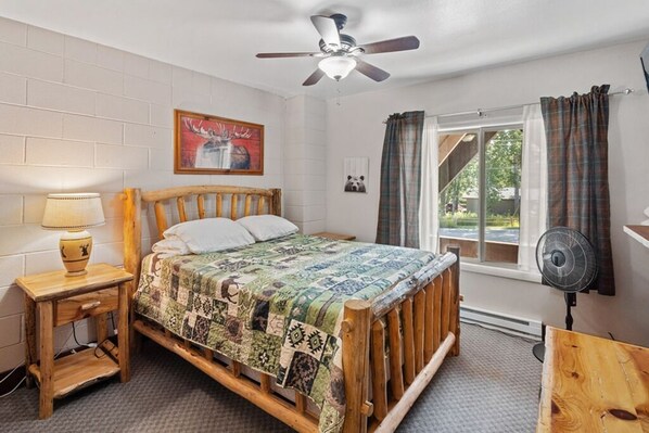 A bedroom with a wooden bed, a ceiling fan, a window with curtains, a bedside lamp, and a framed picture on the wall. - Château Rouge 213 ~ Grizzly Peak Getaway (Red Lodge)